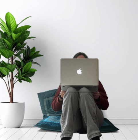 Image of Sara from Your Savvy Studio sitting on the floor on some cushions with a laptop on her knees working on social media graphics for wellness businesses